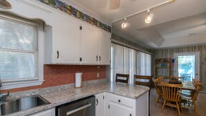 Una cocina con armarios blancos, encimera de granito, lavavajillas y un comedor con sillas de madera y una mesa.