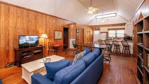 Un salon spacieux avec un canapé bleu, un plancher en bois, un téléviseur et un coin repas comprenant des chaises et une table.
