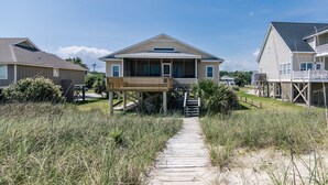 Une propriété située en bord de mer, dotée d’une terrasse en bois, d’une allée couverte et offrant une vue sur l’océan.