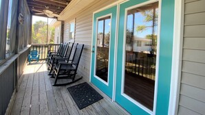 A covered porch with wooden flooring, a row of rocking chairs, and a ceiling fan. - Third-Row Home w/ Ocean Views & Easy Beach Access; Screened Porch; Sun Deck; CableTV/WiFi (Edisto Beach)