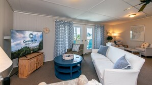 A living room with a television, a round coffee table, a white sofa, and a patterned curtain. - Third-Row Home w/ Ocean Views & Easy Beach Access; Screened Porch; Sun Deck; CableTV/WiFi (Edisto Beach)