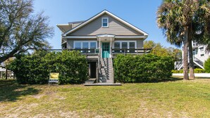 A two-story house with a front porch, a staircase leading to the entrance, and a signboard. - Third-Row Home w/ Ocean Views & Easy Beach Access; Screened Porch; Sun Deck; CableTV/WiFi (Edisto Beach)