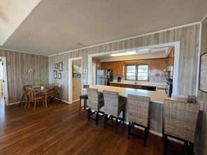 A modern kitchen with wooden cabinets, a marble countertop, and a dining area with wicker chairs.