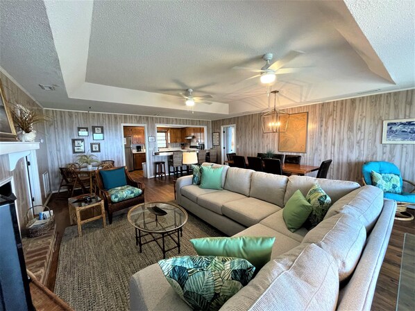 A spacious living room with a large sofa, a dining area, and a kitchen in the background.
