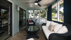 Eine überdachte Veranda mit Deckenventilator, einem Korbsessel, einem Glastisch und Blick ins Freie.