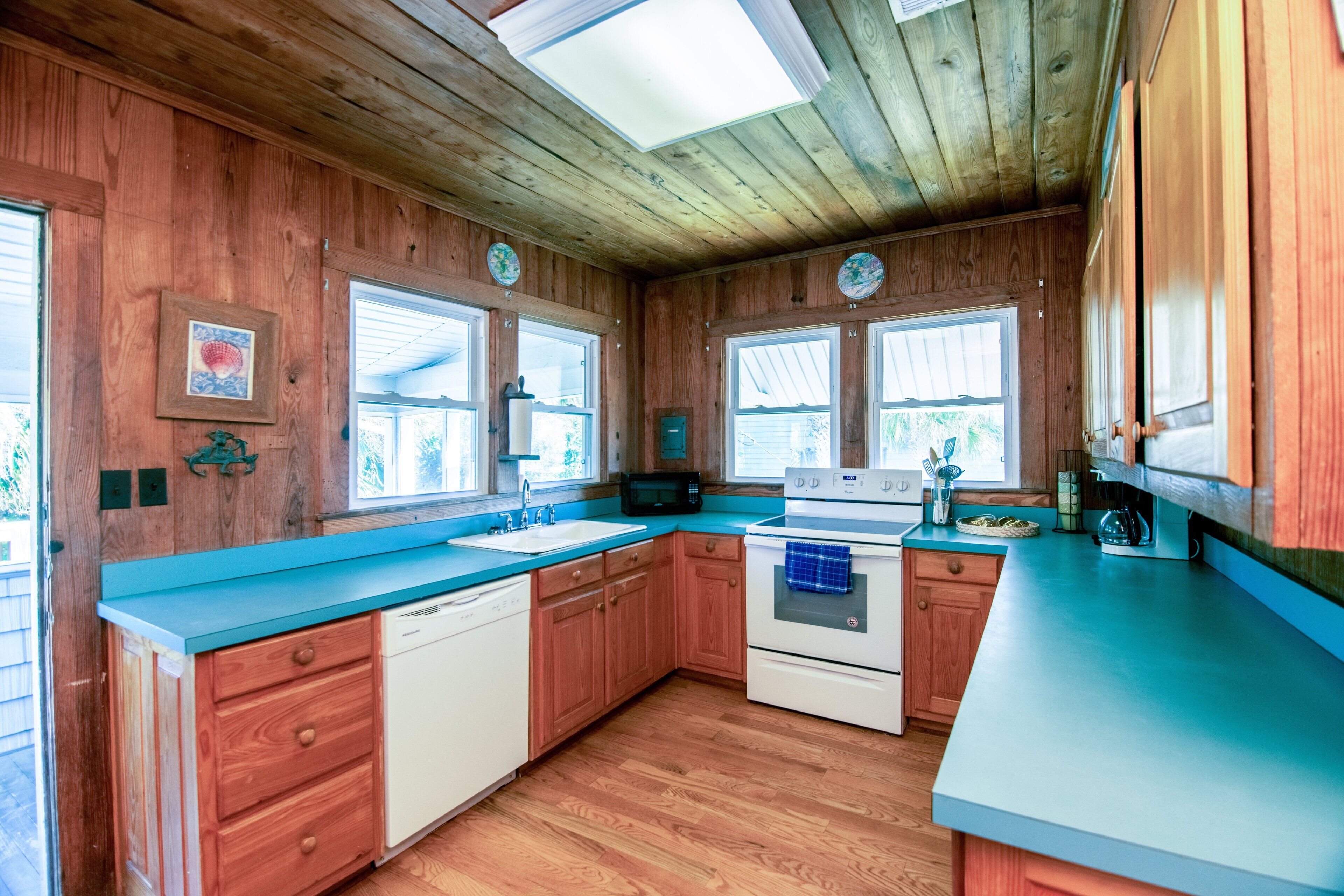 A kitchen with wooden walls, a blue countertop, and a white dishwasher.