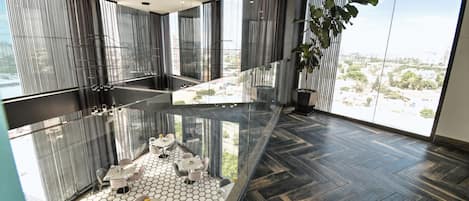 A modern interior with a glass floor, a dining area with tables and chairs, and a large window offering a city view.