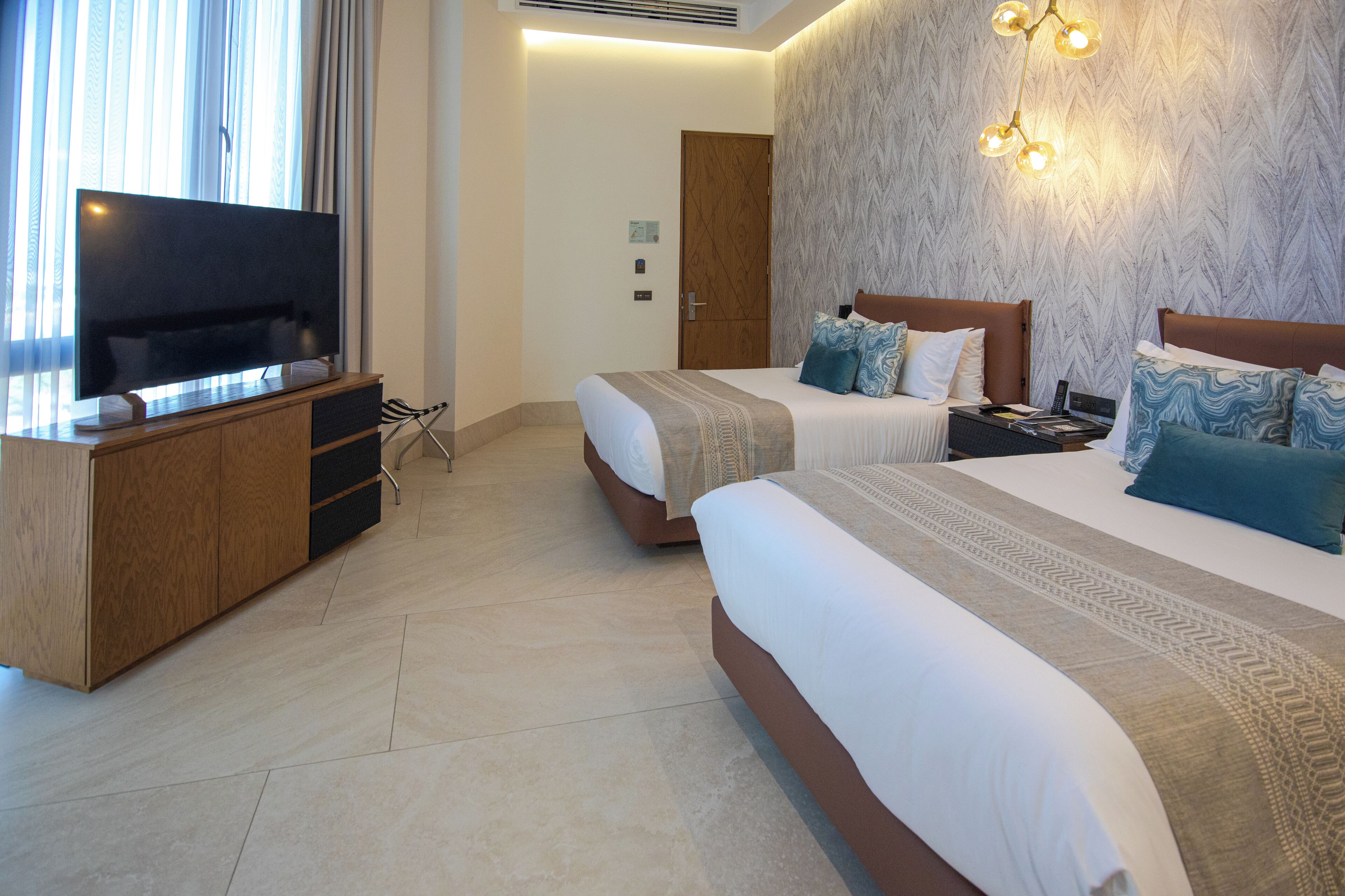 A hotel room with two beds, a TV, a wooden cabinet, and a wall-mounted light fixture.