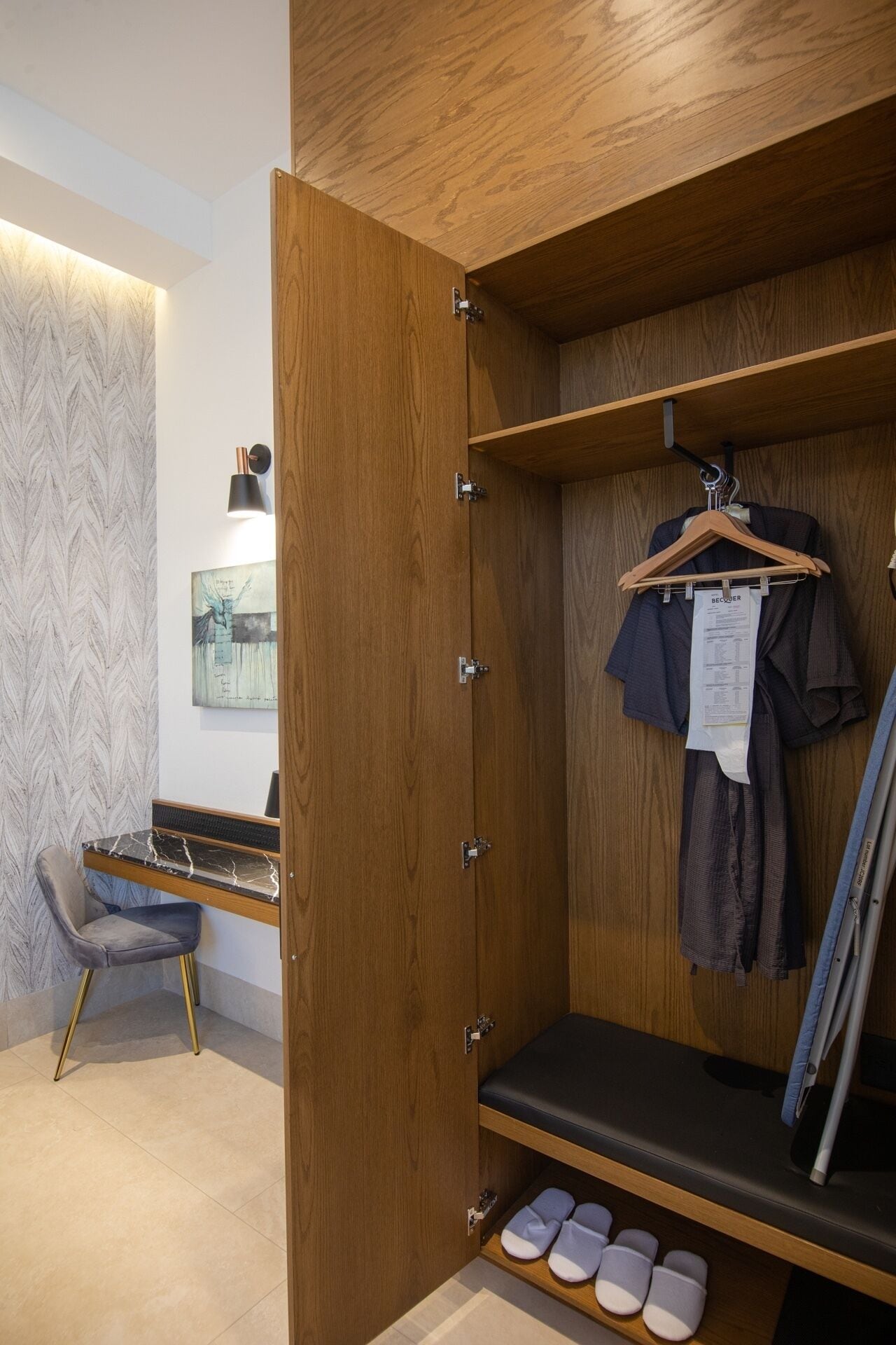 A wooden wardrobe with a bench, a hanging rack, and a pair of slippers on the floor.