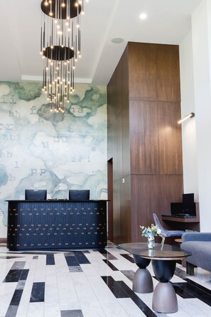 Un vestíbulo moderno con piso a cuadros, una recepción de color azul oscuro, una mesa redonda de vidrio y un panel de madera vertical.