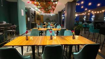 A restaurant with wooden tables and teal chairs, string lights, and hanging paper birds.
