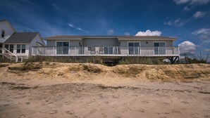 Een strandhuis met een balkon, een garage en een zandstrand op de voorgrond.