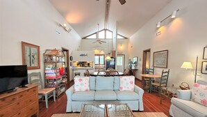 A spacious living room with a sofa, coffee table, and a television on a wooden dresser.