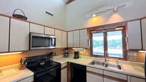 A compact kitchen with a microwave, stove, dishwasher, and a window with a view.