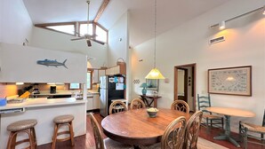A dining area with a wooden table and chairs, a kitchen in the background, and a ceiling fan.