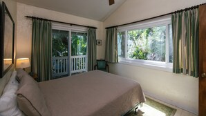 Ein Schlafzimmer mit einem Bett, einem Deckenventilator, einem Fenster mit Vorhängen und Blick ins Grüne.