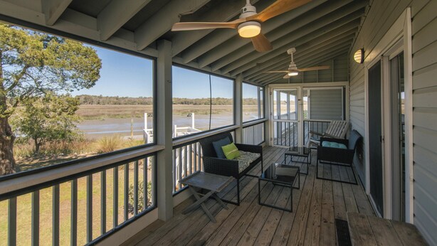 Eine überdachte Veranda mit Holzboden, Deckenventilatoren und Sitzbereichen mit Kissen.