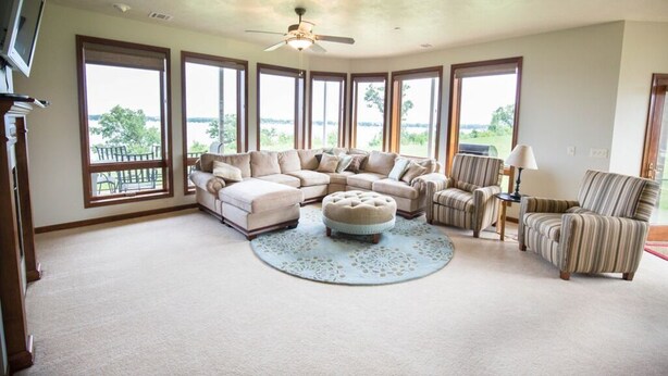A spacious living room with a large L-shaped sectional sofa, a round ottoman, and a striped armchair. - Prime Lakefront East Okoboji Condo at Bridges Bay Jet Ski Lift rental available! (Arnolds Park)