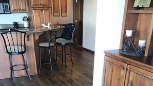 A kitchen with wooden flooring, a dining area with two chairs, and a cabinet with a candle holder. - Prime Lakefront East Okoboji Condo at Bridges Bay Jet Ski Lift rental available! (Arnolds Park)