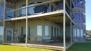 A two-story building with a covered patio area, outdoor seating, and a grill. - Prime Lakefront East Okoboji Condo at Bridges Bay Jet Ski Lift rental available! (Arnolds Park)