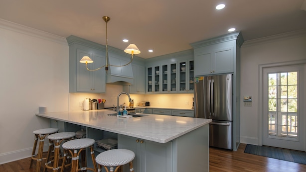 Una cocina con una isla grande, taburetes de bar, un refrigerador de acero inoxidable y armarios azul claro.