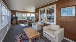 A spacious living room with a large window, a television, a wooden coffee table, and a patterned rug.