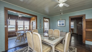 A dining area with a glass-top table, striped chairs, and a ceiling fan.