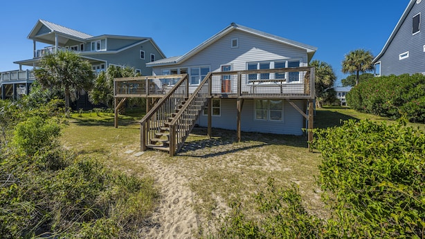 A beachfront property with a two-story house, a wooden deck, and a staircase leading to the upper level.