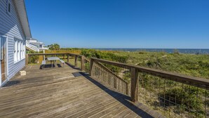 A wooden deck with a table and chairs, overlooking a beach with a clear sky.