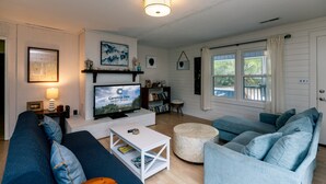A living room with a TV, sofas, a coffee table, and a fireplace. - Villa Kunterbunt | Classic Beach Walk Cottage | Screened Porch & Sun Deck | Sleeps 8 | Pet Friendly (Edisto Beach)