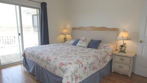 Ein Schlafzimmer mit blumigem Bettbezug, Holzboden, einer Schiebetür aus Glas und zwei Nachttischlampen.