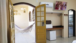 Ein Zimmer mit Hängematte, Bett, kleinem Kühlschrank und Fernseher an der Wand.