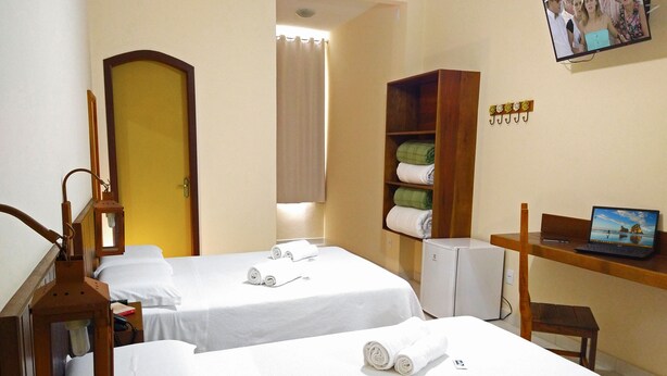 Ein Hotelzimmer mit zwei Betten, einem Fernseher auf einer Holzablage, einem kleinen Kühlschrank und einem Holzschrank mit Handtüchern.