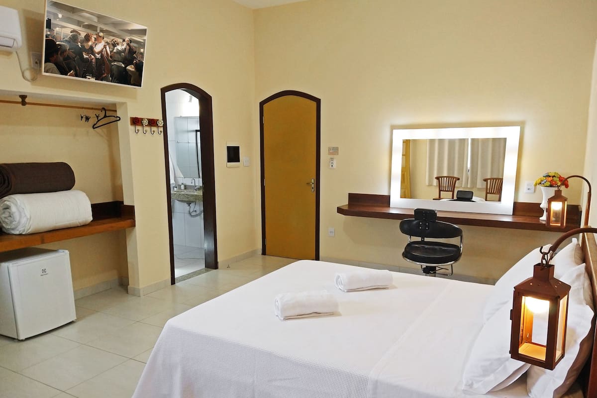 Une chambre d’hôtel comprenant un lit, un petit réfrigérateur, un miroir, une chaise et une table de chevet avec une lampe.