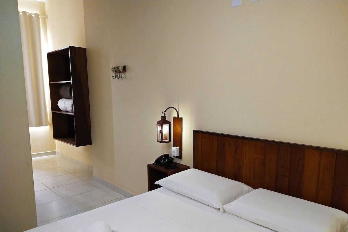 Une chambre d’hôtel comprenant un lit, une table de chevet avec une lampe, un téléphone et une étagère avec des serviettes.