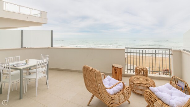 A balcony with a view of the beach, wicker furniture, and a table with chairs.