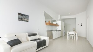 A modern apartment with a white sofa, a kitchen with a wooden countertop, and a dining area.