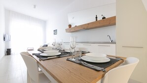 A modern dining area with a wooden table set for four, white chairs, and a kitchen in the background.