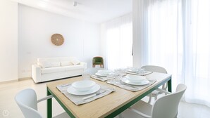 A modern dining area with a wooden table set for four, white chairs, a white sofa, and a green chair. - Rivazzurra Homes - 36 (Termoli)
