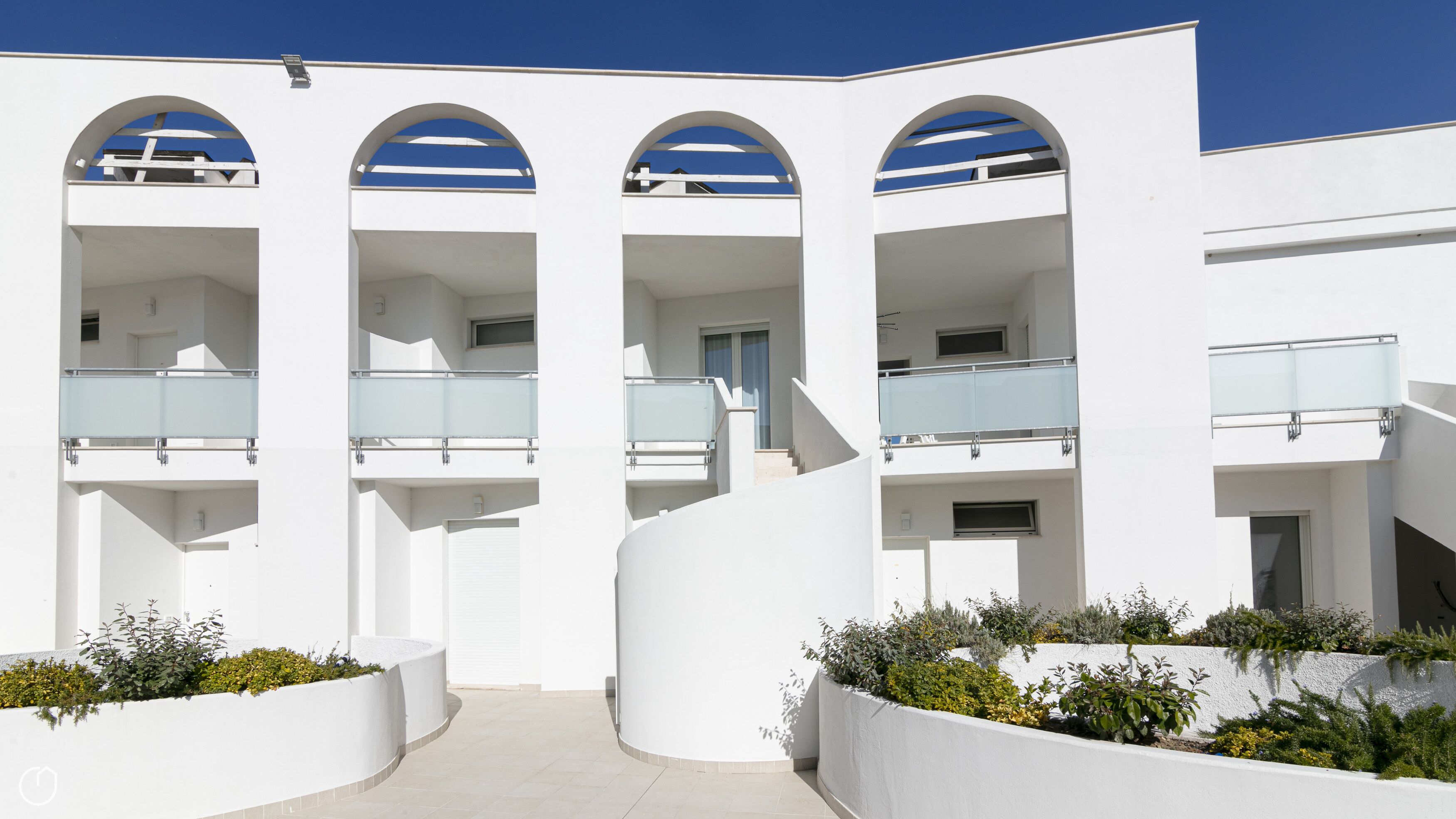Un edificio moderno con tres balcones arqueados, una escalera central y fachada blanca.