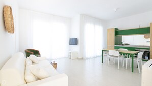 A modern living room with a sofa, a TV, and a dining area with chairs and a table. - Rivazzurra Homes - 36 (Termoli)