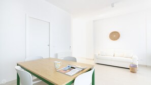Une pièce lumineuse et épurée, avec une table en bois, des chaises blanches, un canapé blanc et un panier en osier.
