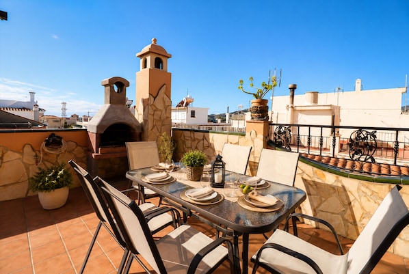 An outdoor patio with a stone oven, a table set for dining, and a view of the cityscape.