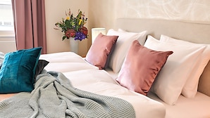 A neatly made bed with a green blanket and multiple pillows, a vase with flowers, and a lamp on a bedside table. - Spacious Old Town Square Apartment (Hlavní mesto Praha)