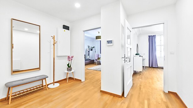 A modern, well-lit room with a wooden floor, a bench, a small table with a potted plant, and a large mirror on the wall. - Spacious Old Town Square Apartment (Hlavní mesto Praha)
