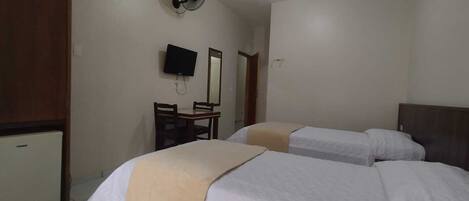 Hotelkamer met twee bedden, een bureau, een stoel, een televisie en een plafondventilator.
