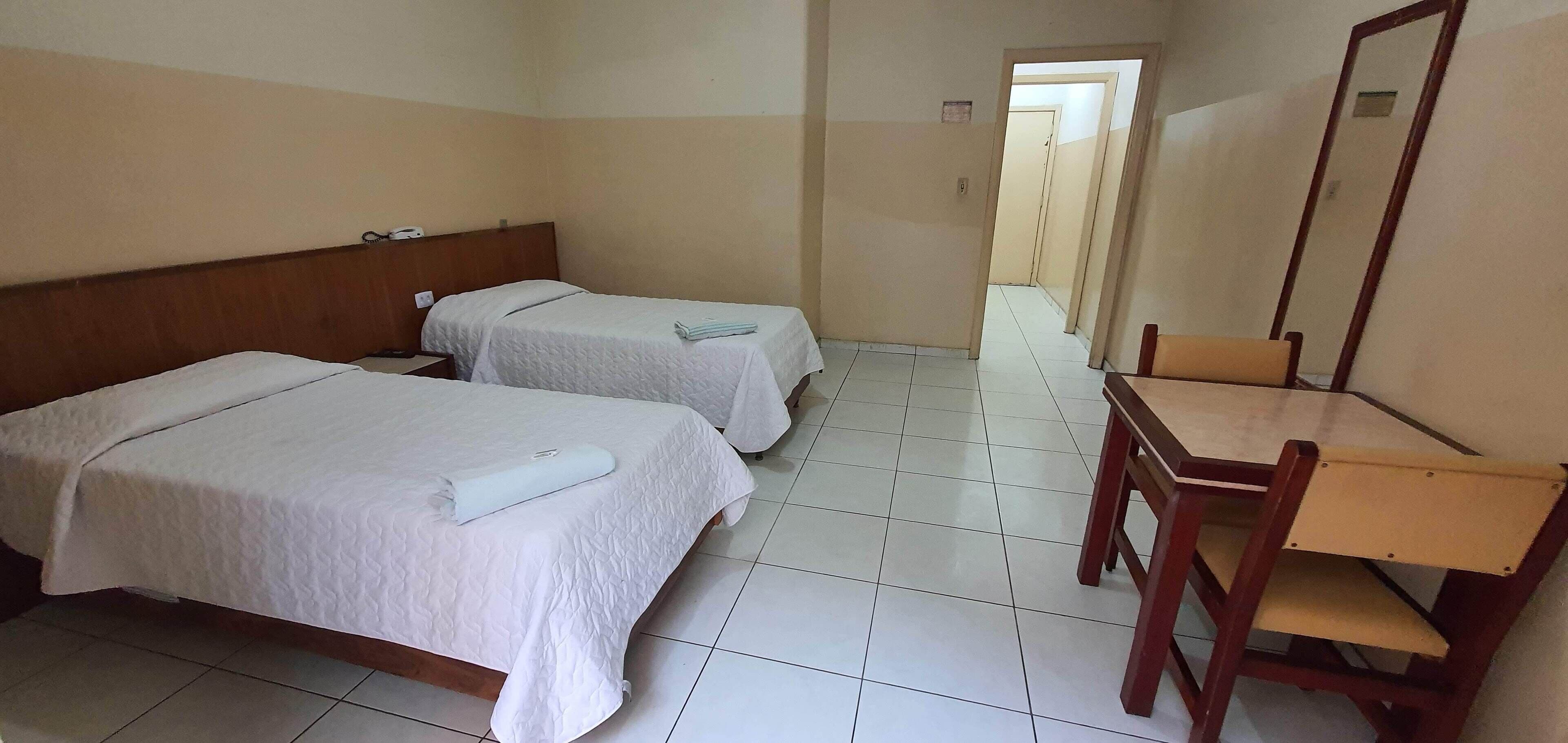 A hotel room with two beds, a wooden desk, and a chair.