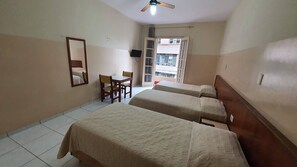 Ein Hotelzimmer mit zwei Betten, einem Schreibtisch, einem Sessel, einem Fernseher und einem Fenster mit Blick auf Gebäude.