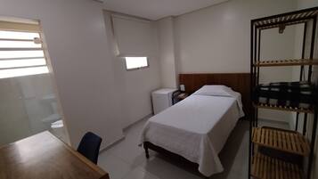 Una habitación pequeña y limpia con cama, escritorio, silla, ventana y espejo.