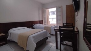 Hotelkamer met twee bedden, een bureau, een stoel, een televisie en een raam met uitzicht op gebouwen.